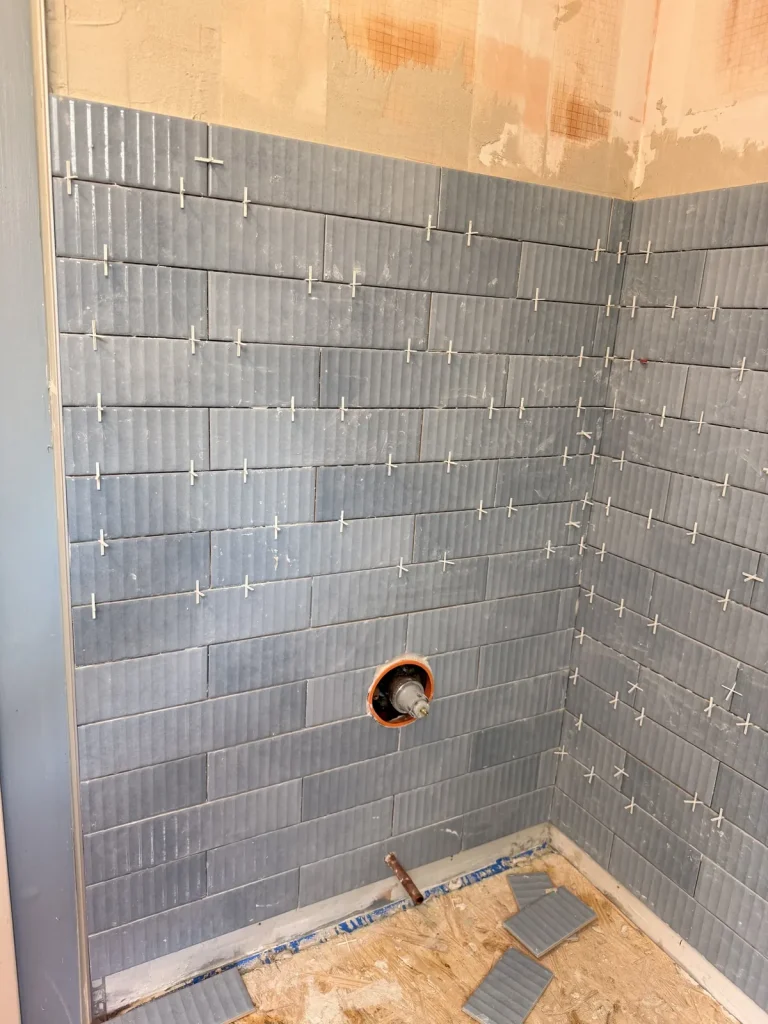 Blue ceramic wall tile being installed in a shower